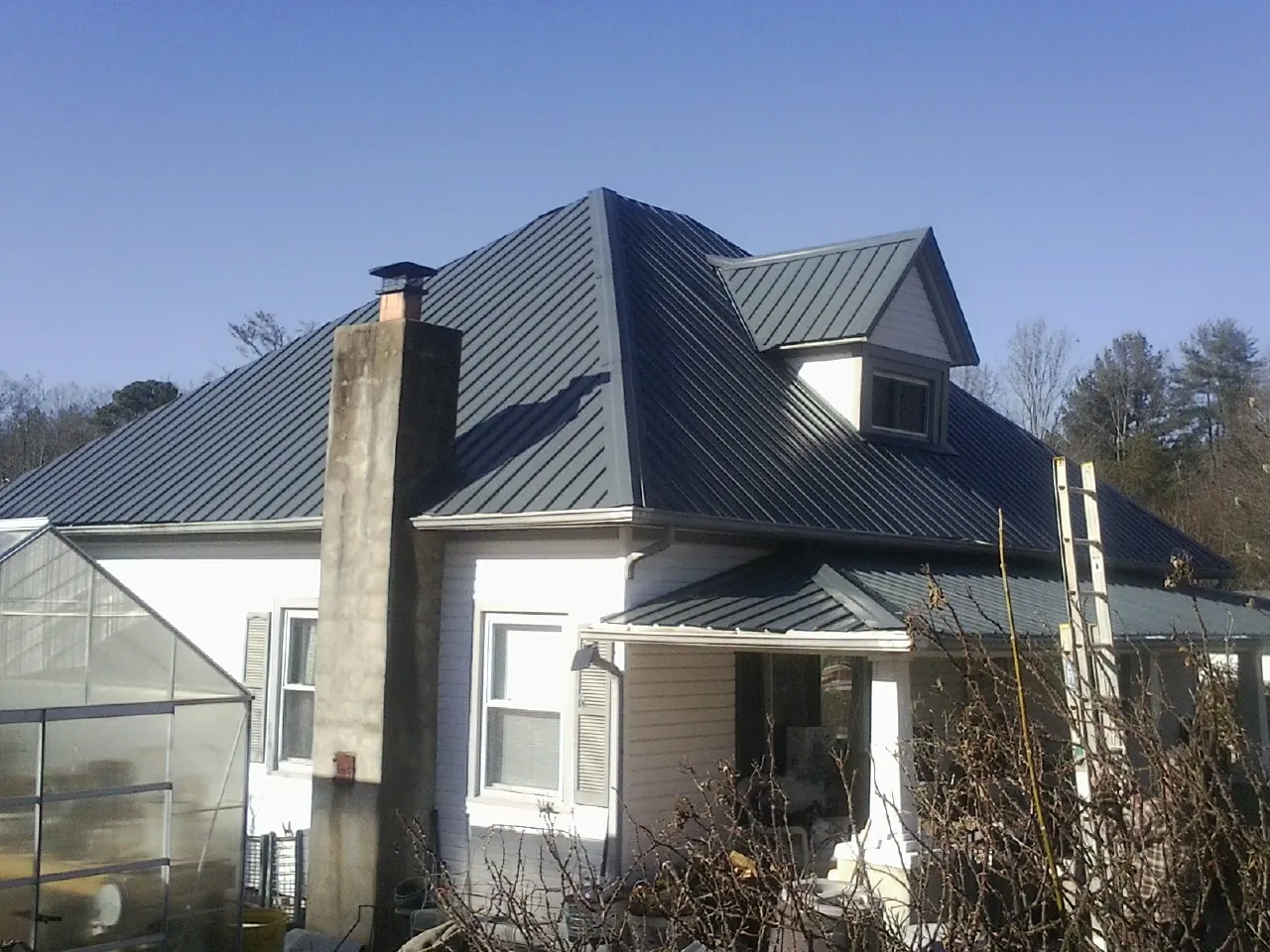 Dark blue standing seam metal roof on a white farmhouse with dormer — Slate & Tile Roof Repair by Roofing Brothers in Greensboro