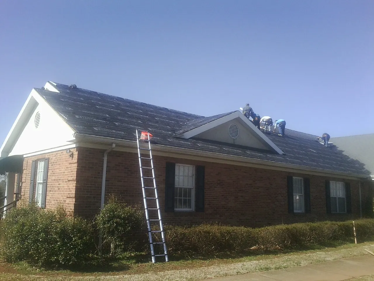 Crew tearing shingles off a brick ranch roof with a ladder set — Metal Roof Repair work by our crew in Greensboro