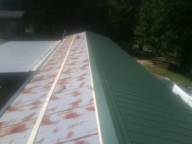 Old rusted panels beside newly installed green metal roofing — Wind Damage Roof Repair by Roofing Brothers in Greensboro