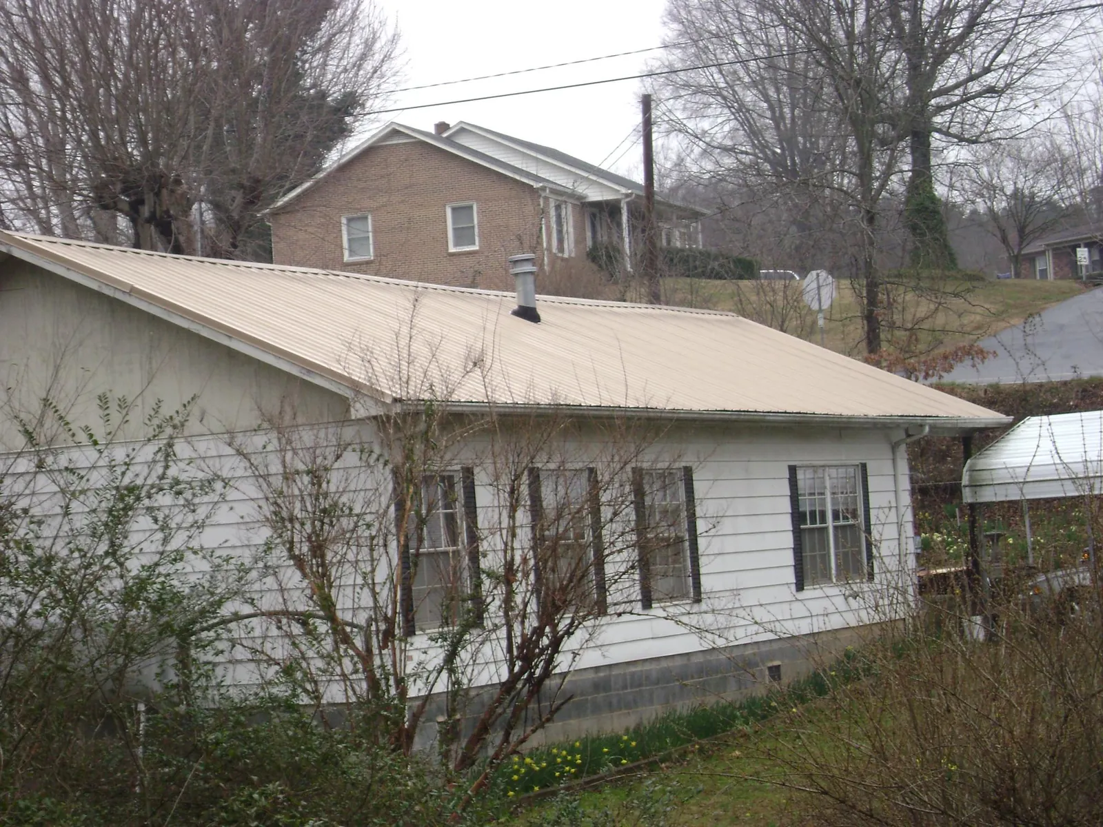 Tan metal roof on a white sided house set into a hillside — Commercial Roofing by Roofing Brothers in Greensboro