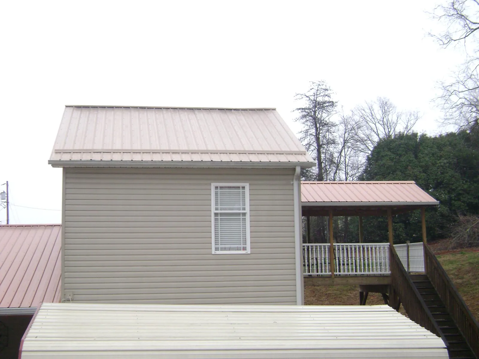 Tan metal roofs on a two story addition and attached porch, from a Roof Replacement job in Greensboro